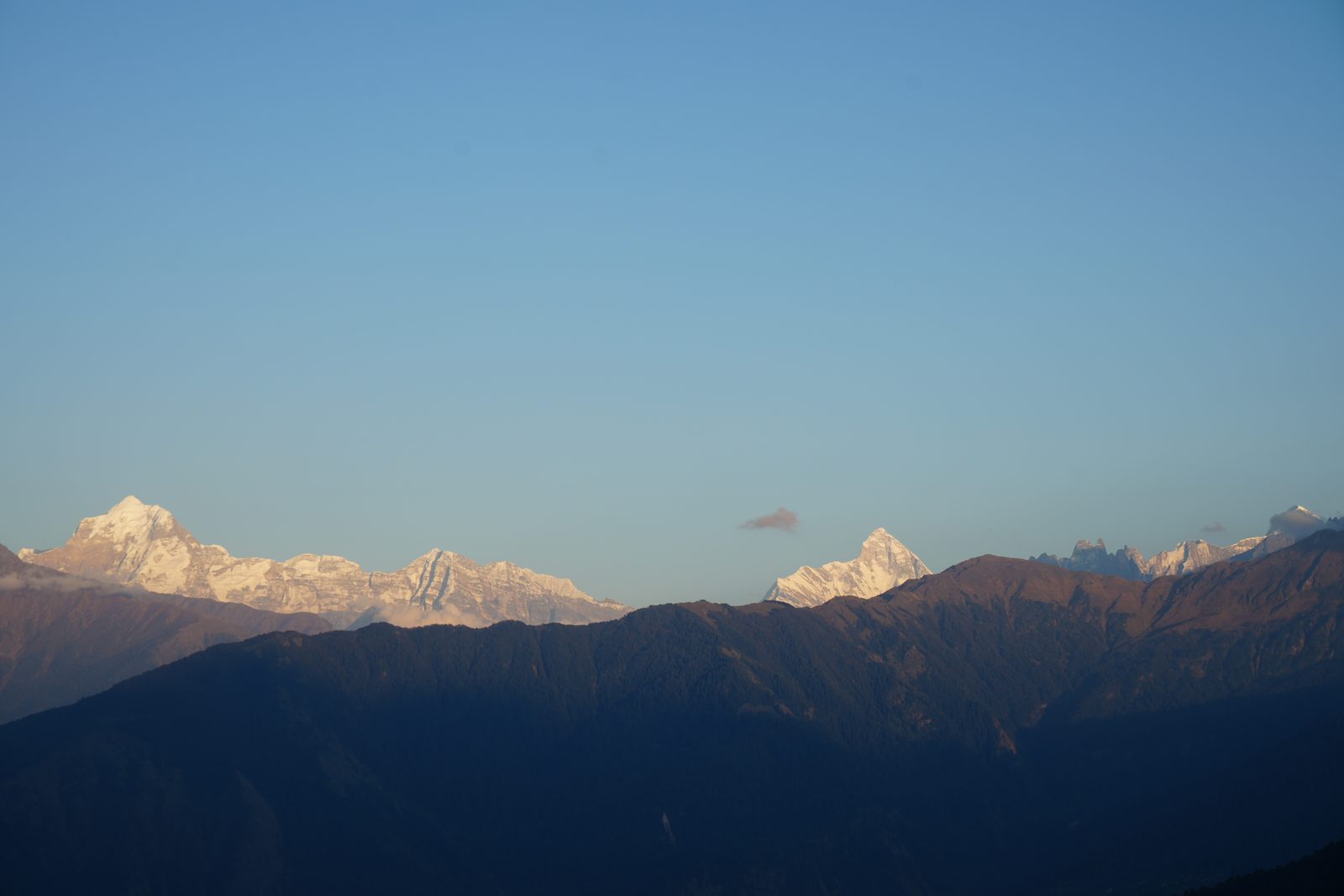 Distant snow summits catching first light above a long dark ridgeline.