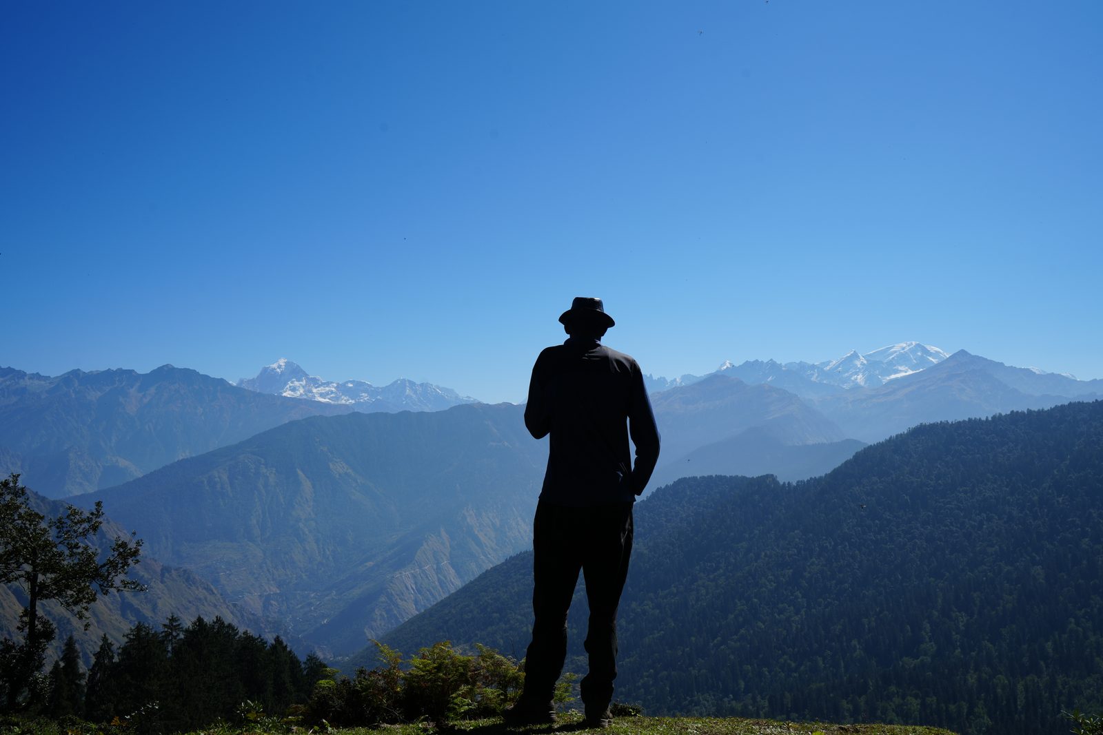 A figure standing to the open range at midday, the snow line behind.
